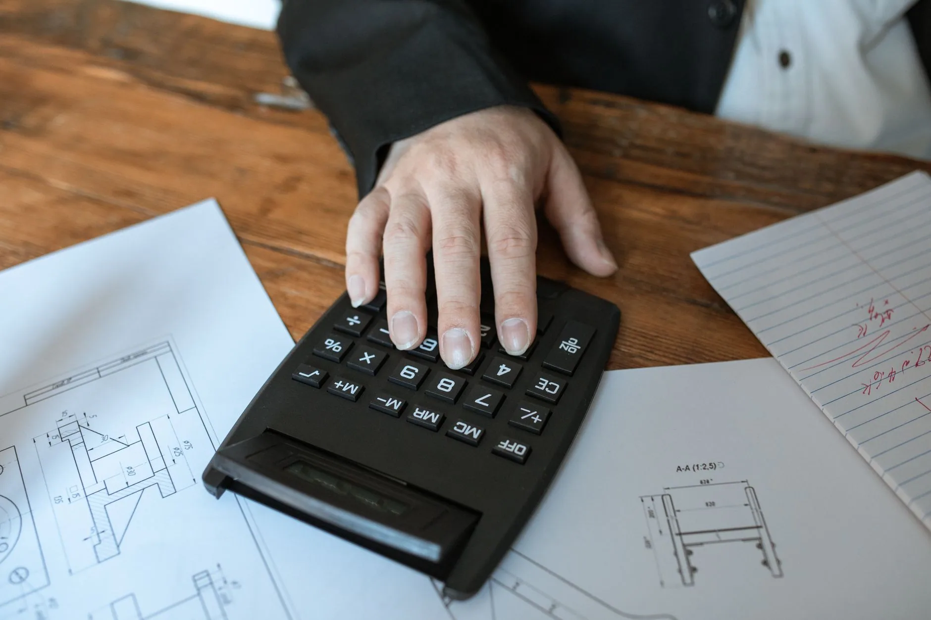 Une main utilisant une calculatrice posée sur des plans